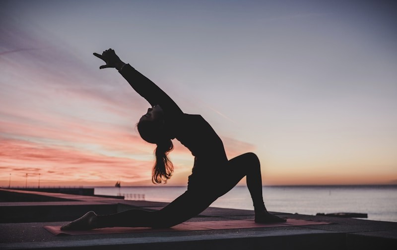 Silhouette of a person in a yoga backbend on a mat at sunset beside the ocean